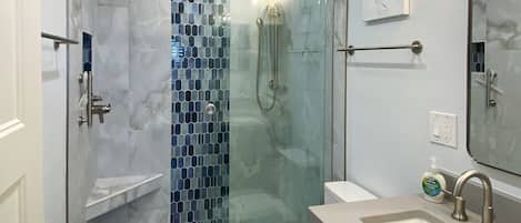 Un baño moderno con ducha de vidrio, inodoro blanco y tocador con lavamanos y espejo.