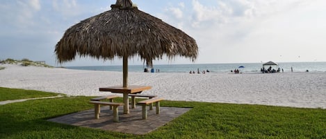 Une plage avec un parasol en chaume et des tables de pique-nique.