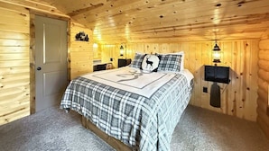 Une chambre à coucher confortable, aménagée dans un style rustique, avec une couvre-lit à carreaux, deux lampes fixées au mur et une porte située sur le côté gauche.