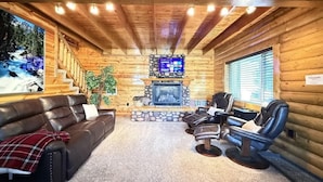 L’intérieur chaleureux d’un chalet en bois, avec une cheminée, des fauteuils en cuir et une vue imprenable sur un paysage enneigé.