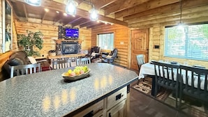 L’intérieur d’une cabane en rondins, avec un îlot central en granit, une table à manger en bois et une cheminée en pierre.