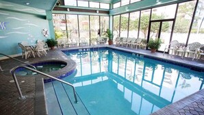 An indoor swimming pool with a hot tub, surrounded by chairs and potted plants.