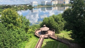 A lakeside view with a gazebo, a wooden deck, and modern buildings in the background.