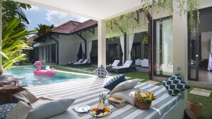 A poolside area with lounge chairs, a dining setup with a fruit platter, and a pink flamingo float. - Villa Alice Satu by Villa Finder (Seminyak)