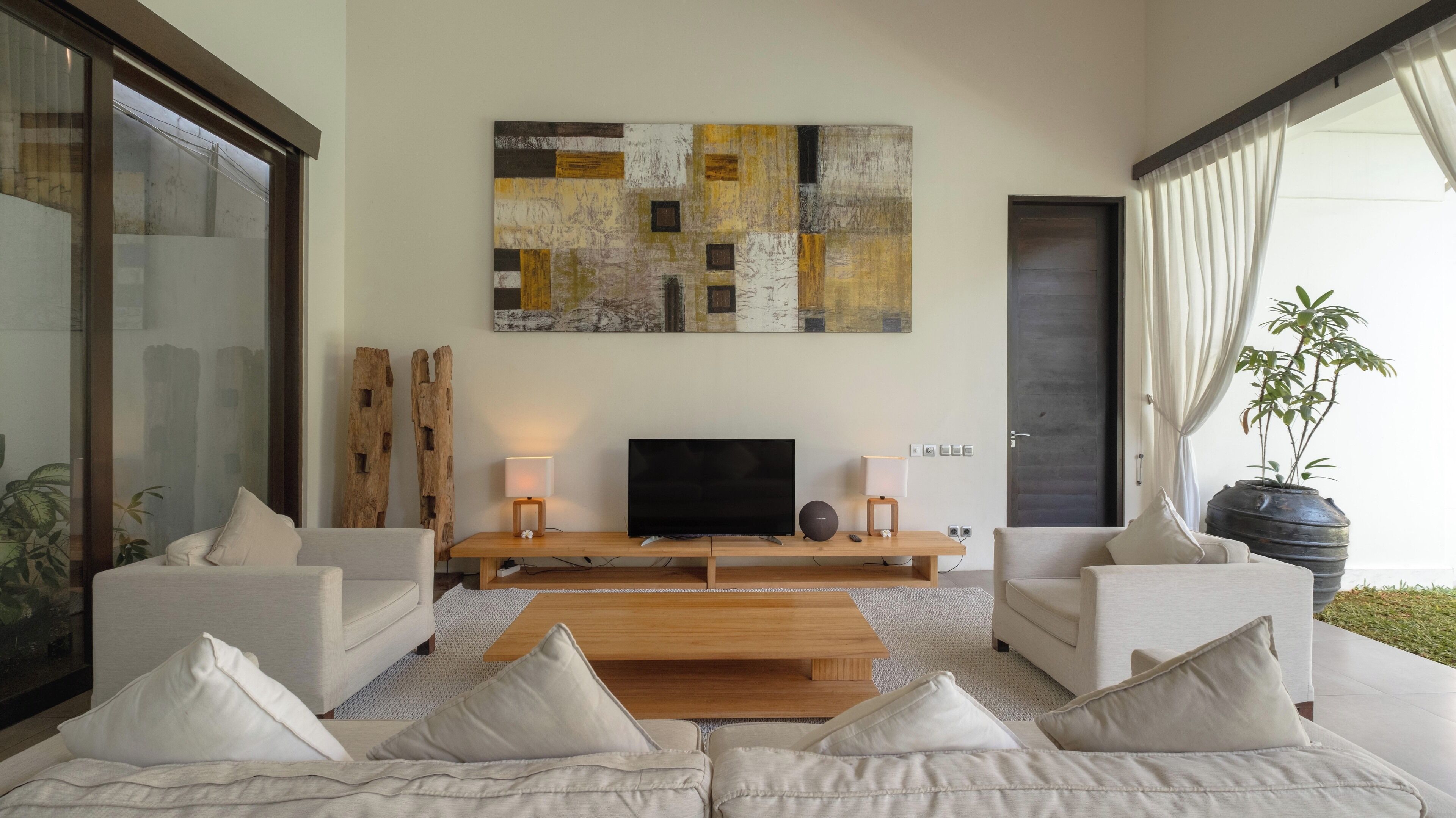 Ein modernes Wohnzimmer mit Flachbildfernseher, zwei Beistelltischen inklusive Lampen, einem Holztisch als Couchtisch und zwei Sofas mit Kissen.