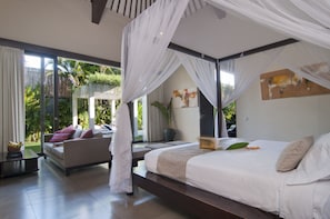 Relax in a serene space with a large bed, sofa, and potted plant, offering a peaceful view of the outdoors.