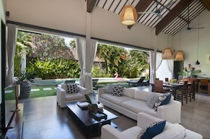 Relax in a spacious living area with a sofa set and coffee table, overlooking a lush garden and pool.