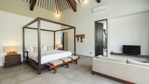 A modern bedroom with a four-poster bed, a sofa, a TV, and a bathroom visible through an open door. - Villa Alice Satu by Villa Finder (Seminyak)