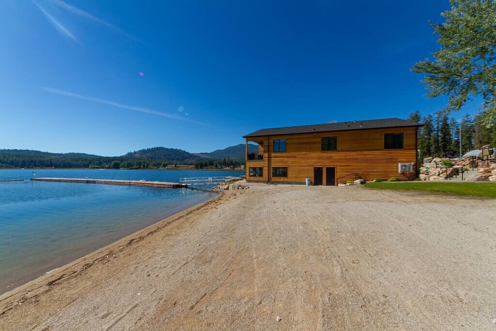 A wooden cabin by a lake with a dock, surrounded by hills.