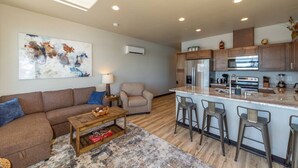 A modern kitchen with a central island, bar stools, and a dining area with a sofa and coffee table.