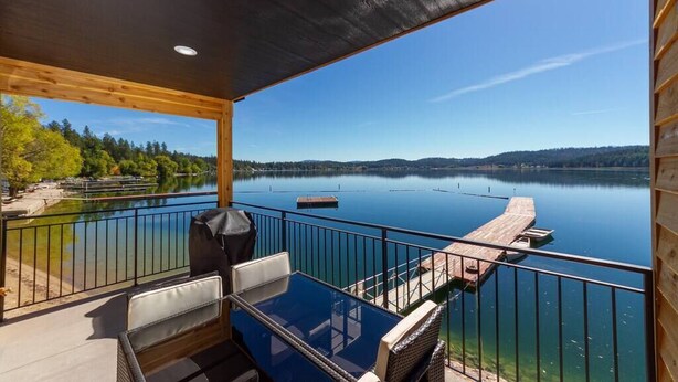 A balcony with a view of a calm lake, wooden deck, and seating area.