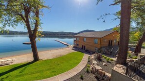 A lakeside property with a wooden house, a dock, and a grassy lawn.