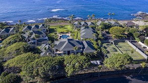An aerial view of a coastal residential area with multiple houses, a tennis court, and a view of the ocean. - POIPU KAPILI 46 - FABULOUS OCEAN VIEWS - WHOLE UNIT AC - WALK TO BEACH/ SHOPPING (Koloa)