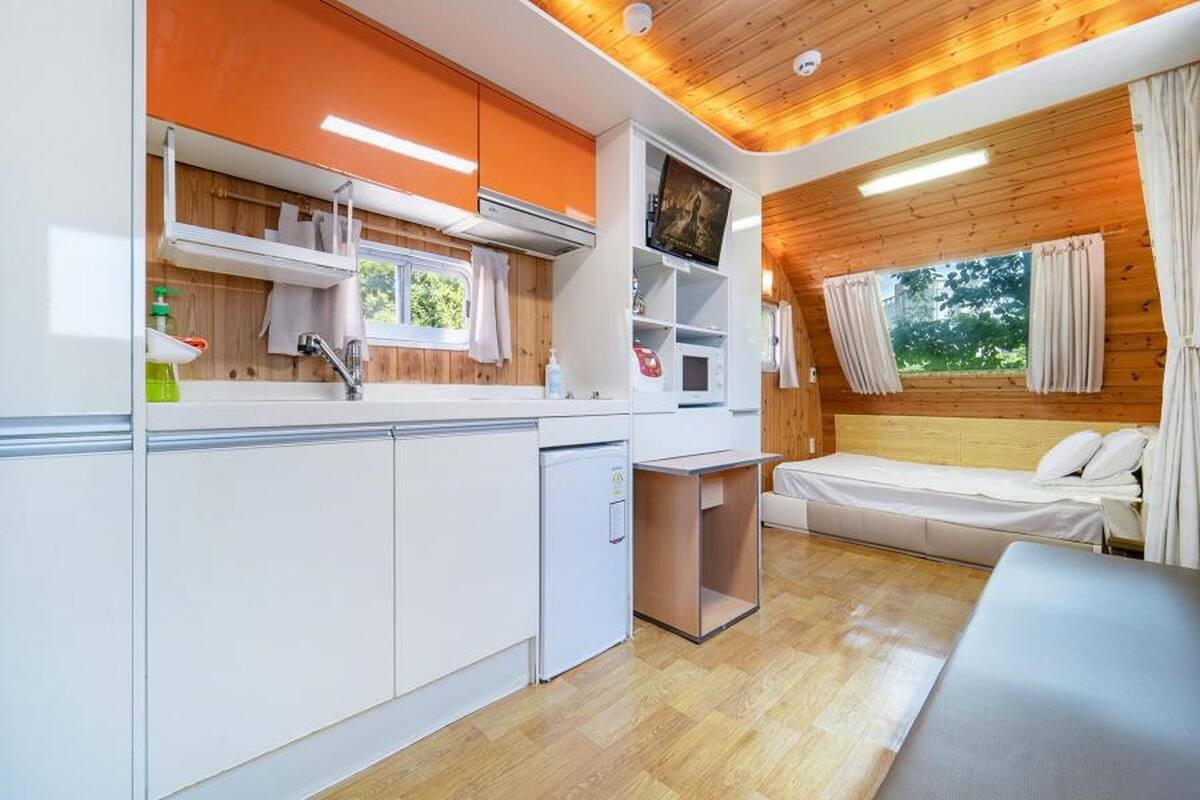 Una cocina compacta con armarios blancos, un refrigerador pequeño y una ventana con cortinas.