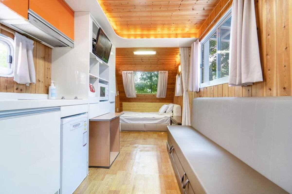 Una cabaña compacta y bien iluminada con kitchenette, una cama y zona de estar.