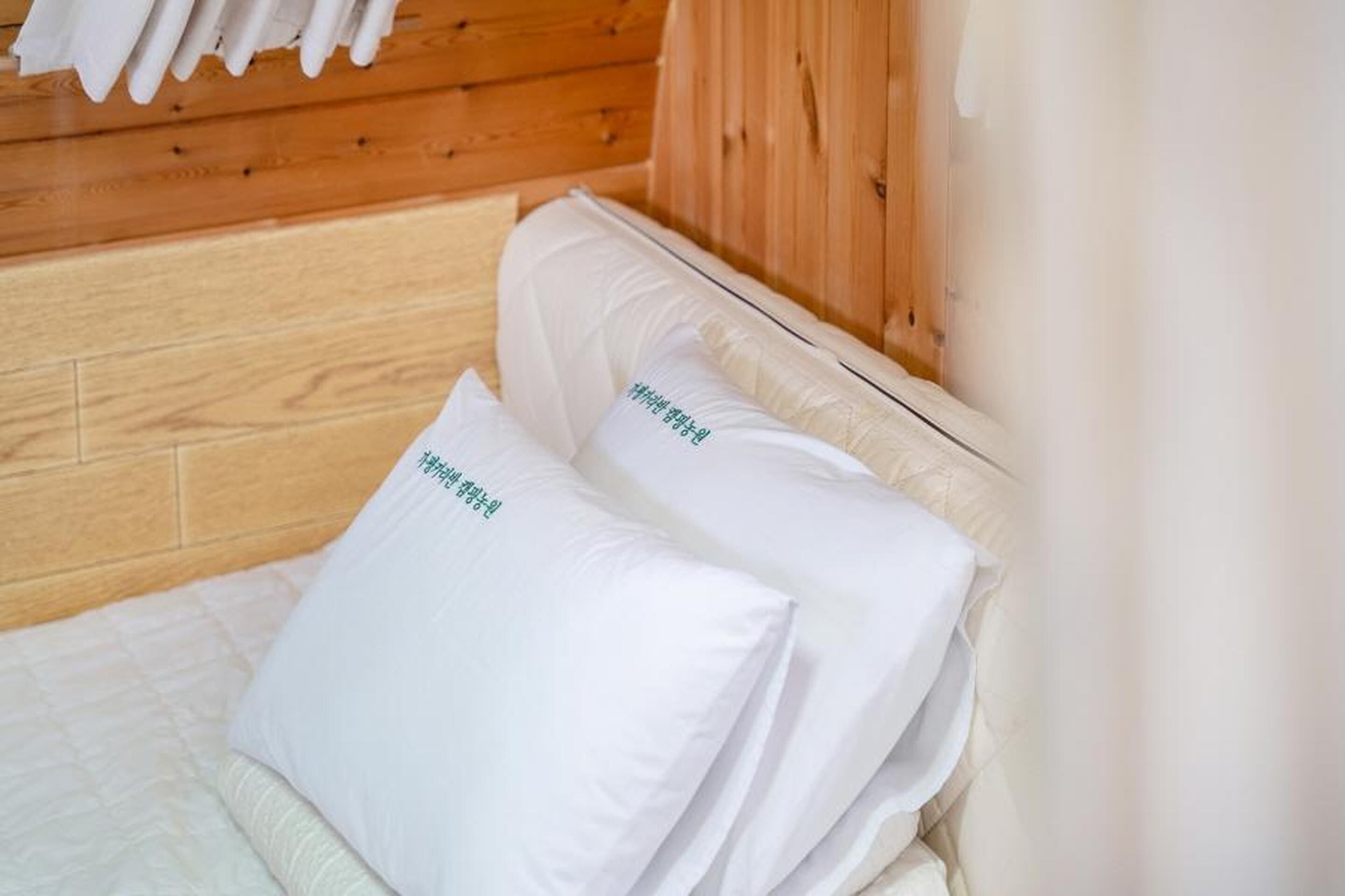 Een houten cabin met een bed, voorzien van witte kussens met groene tekst.