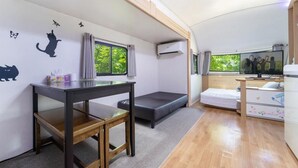 Una habitación compacta con cama, una mesita, ventana con cortinas y detalles decorativos de animales en la pared.