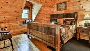 A wooden cabin bedroom with a bed, a desk, a chair, a window, and a ceiling fan. - The Hideaway at Blue Ridge | Blue Ridge, GA (Mineral Bluff)
