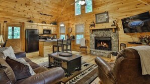 A cabin interior with a stone fireplace, wooden ceiling, and a television mounted on the wall. - The Hideaway at Blue Ridge | Blue Ridge, GA (Mineral Bluff)