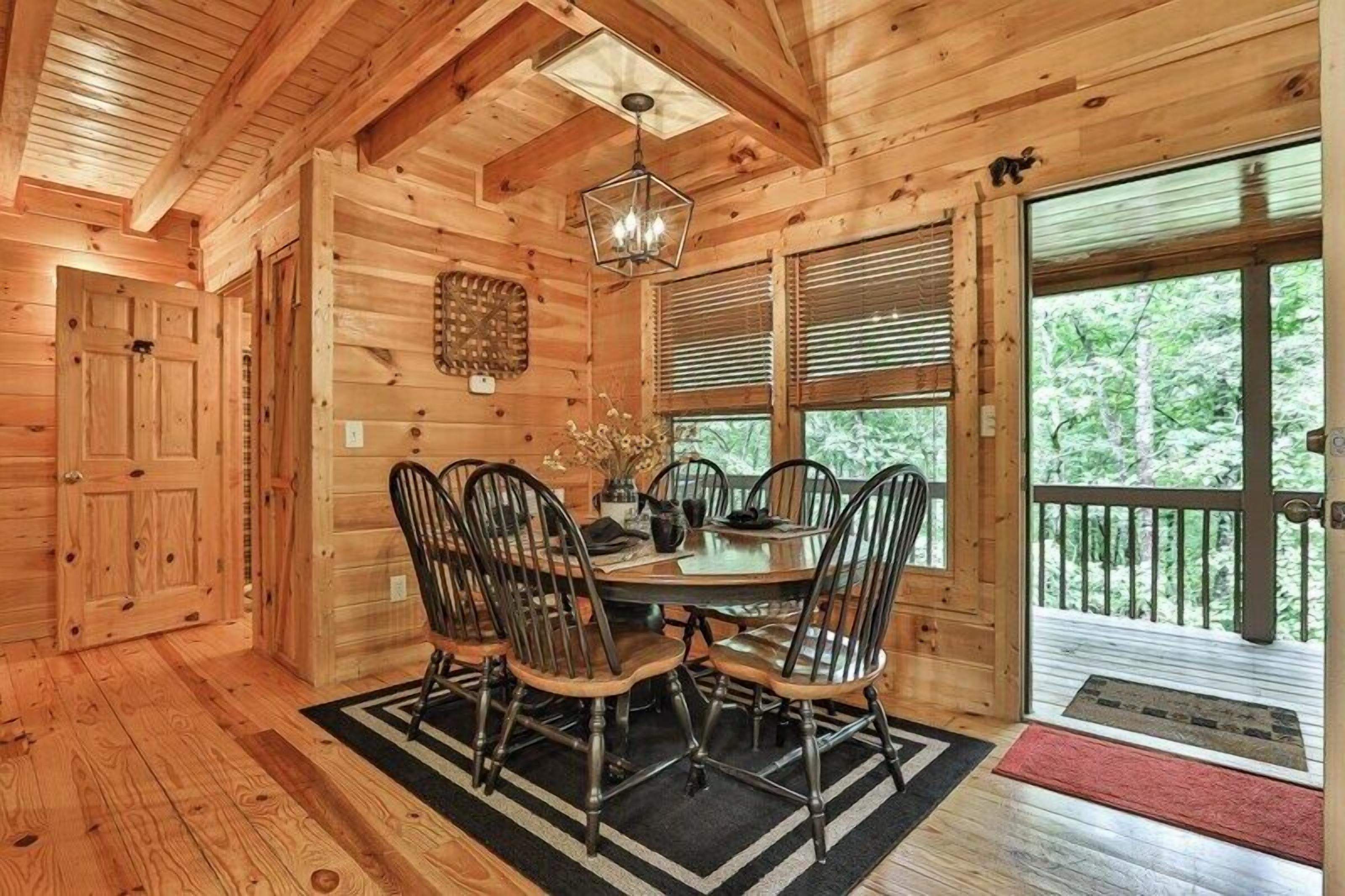 L’intérieur d’un chalet en bois comprend une table à manger, des chaises, un lustre et de grandes fenêtres.
