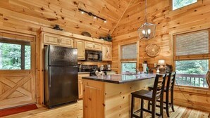A wooden cabin kitchen with a refrigerator, stove, microwave, and bar stools. - The Hideaway at Blue Ridge | Blue Ridge, GA (Mineral Bluff)