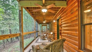 A log cabin with a covered porch, wicker furniture, and large windows offering forest views. - The Hideaway at Blue Ridge | Blue Ridge, GA (Mineral Bluff)