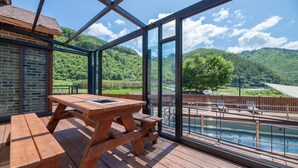 Una terraza de madera con una mesa de picnic que da a una piscina y una vista panorámica de colinas.