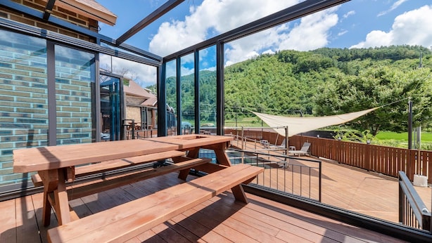 Terraza de madera con mesas de picnic y vistas a una colina boscosa.