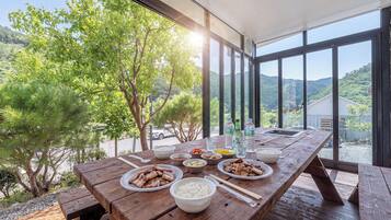 A wooden dining table with various dishes, including rice, meat, and vegetables, set outdoors with a view of a forest and mountains.
