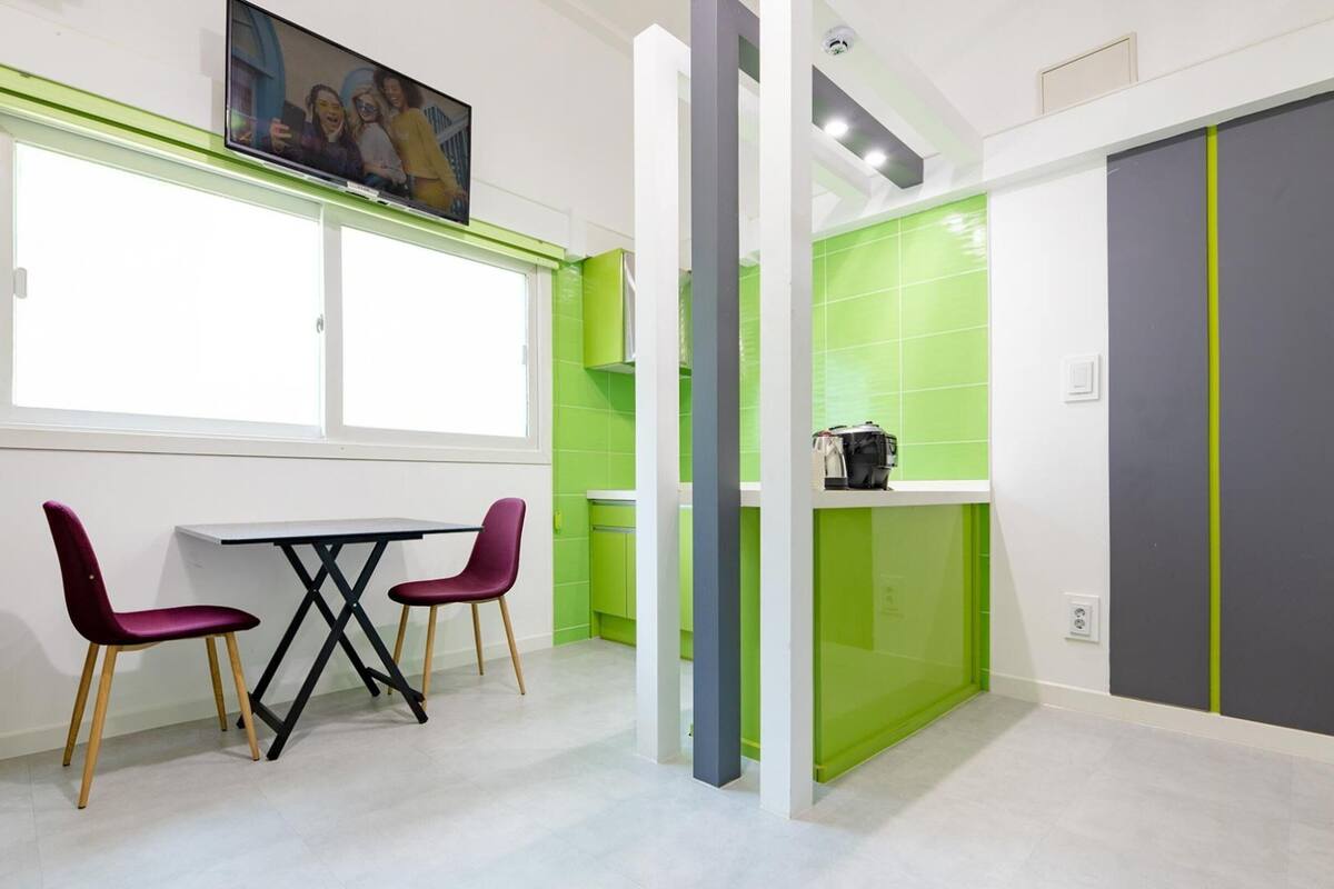Una habitación moderna con una mesa de comedor y sillas, un televisor y una pared de acento verde.
