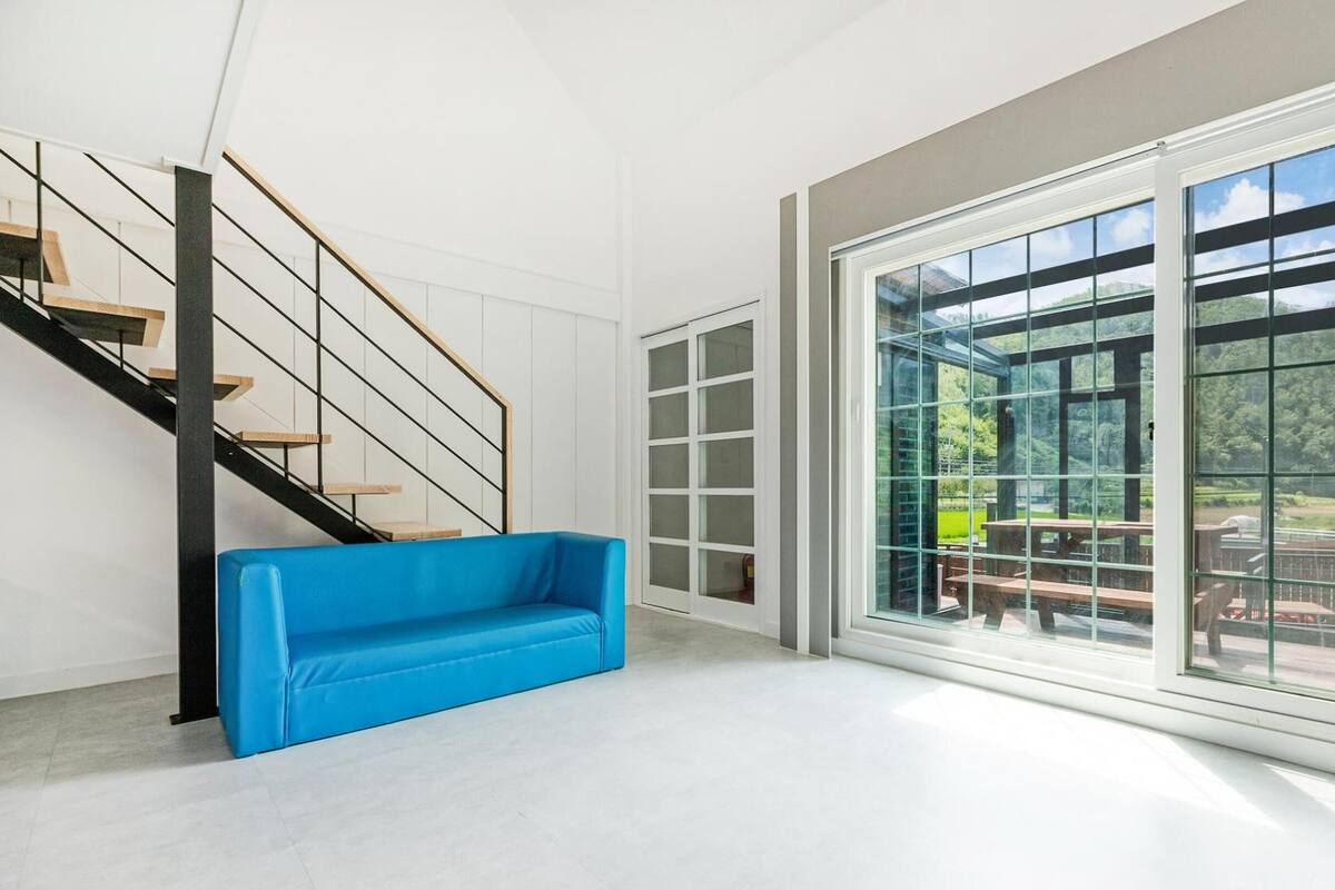 Amplia habitación con una escalera moderna, un sofá azul y grandes puertas correderas de vidrio que dan a un área exterior con un patio.