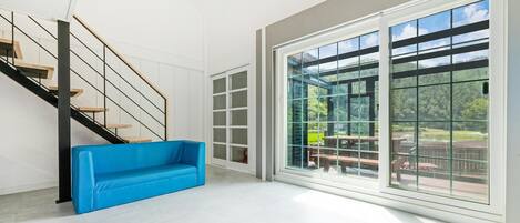 A spacious room with a modern staircase, a blue sofa, and large sliding glass doors leading to an outdoor area with a patio.