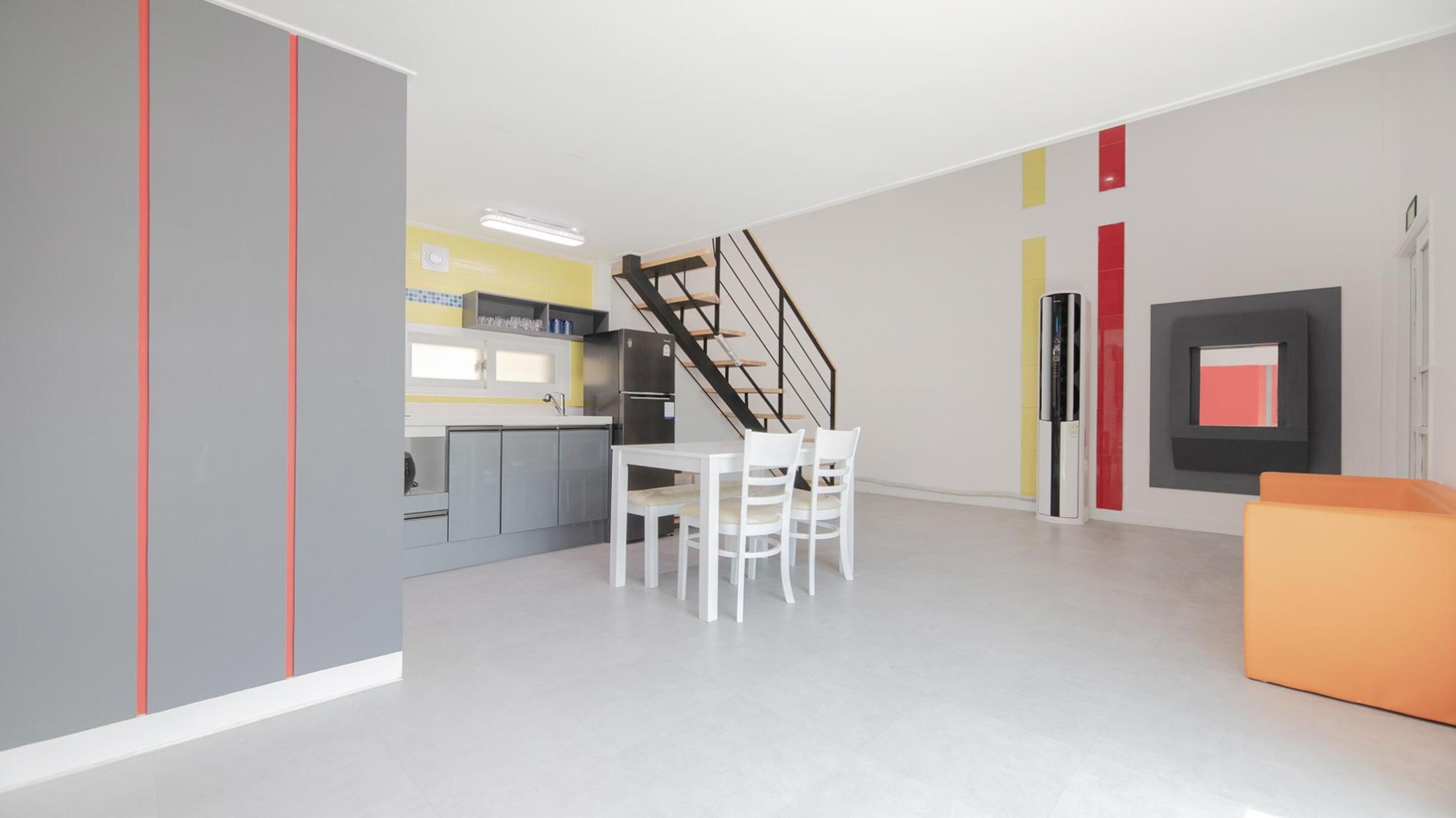 A modern kitchen with a dining area, a staircase, and a living space with a sofa.