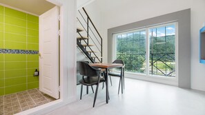 Una habitación moderna con pared de azulejos verdes, una mesa de madera con dos sillas, una escalera y un ventanal con vistas a la vegetación.