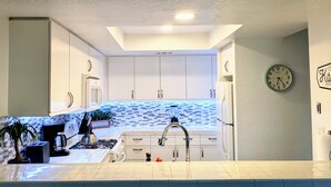 A modern kitchen with white cabinets, a tiled backsplash, a sink, and a clock on the wall.