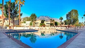 A rectangular pool with clear blue water, surrounded by lounge chairs and palm trees, with a mountain in the background.