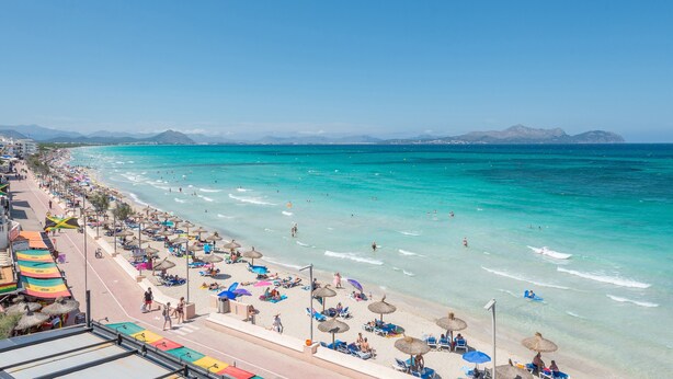 Een strand met helder turquoise water, parasols en strandstoelen.