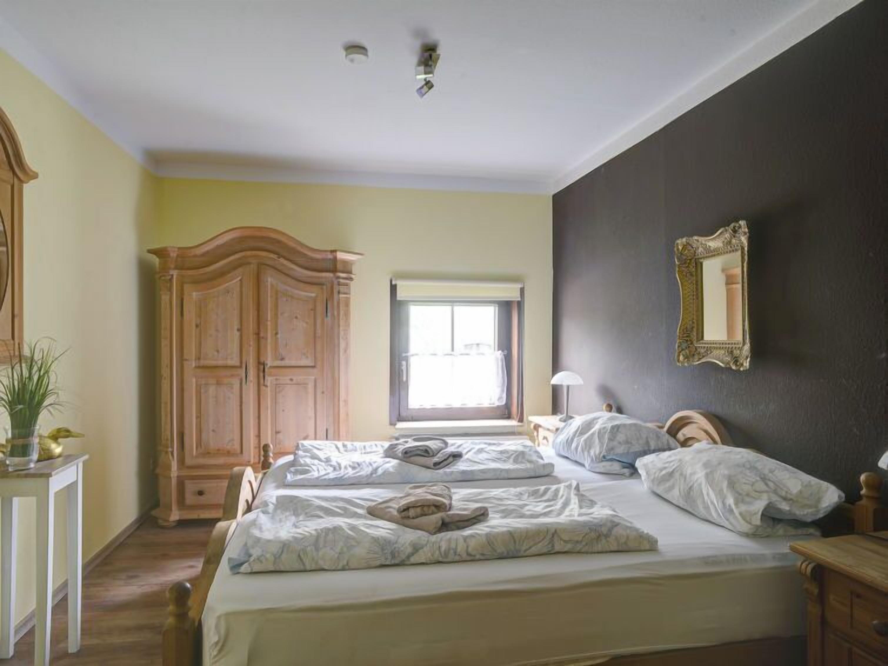 A bedroom with two beds, a wardrobe, a window, and a mirror on the wall.