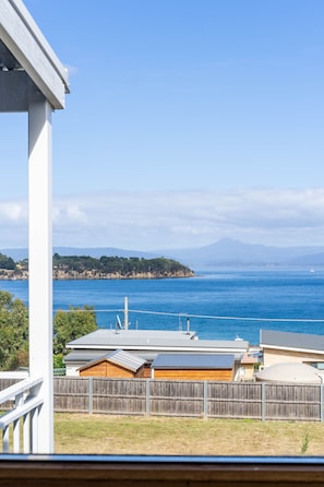A coastal view with a wooden fence, a house with a metal roof, and a clear blue sky.