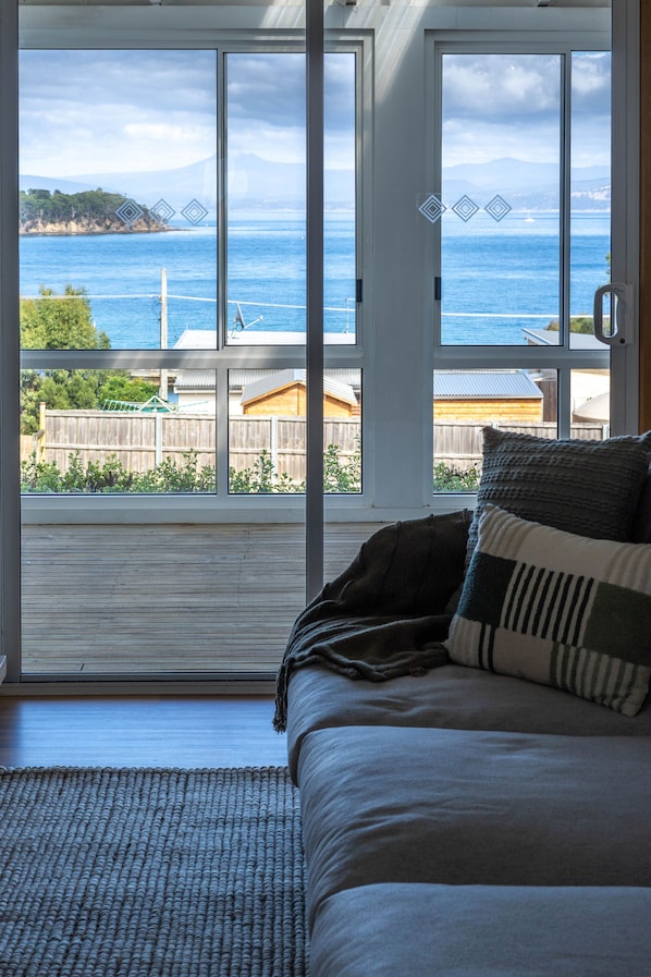 A bedroom with a large sliding glass door leading to a balcony overlooking a body of water and a distant mountain.