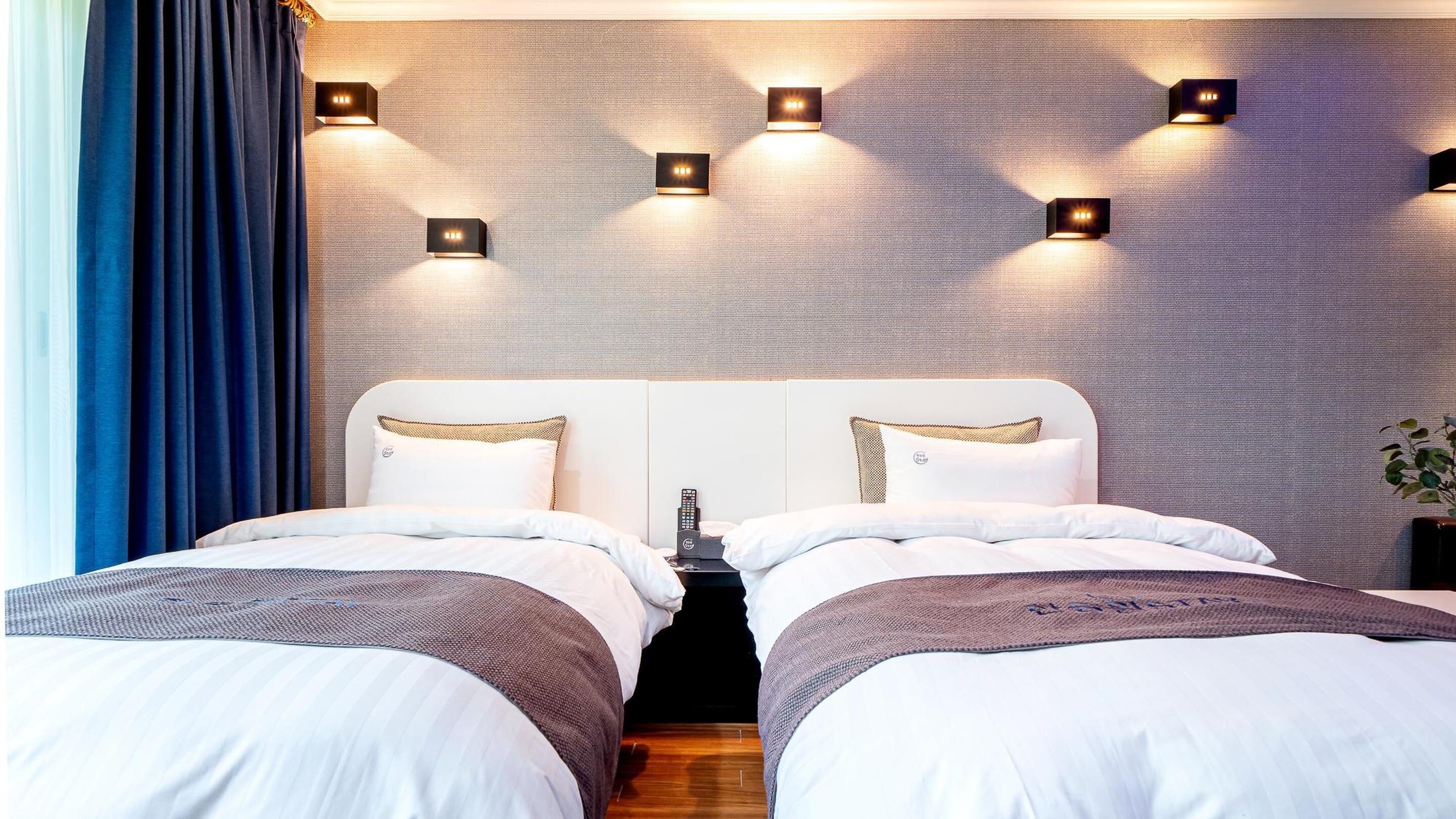 Habitación de hotel con una cama grande, dos mesitas de noche y una lámpara de pared.