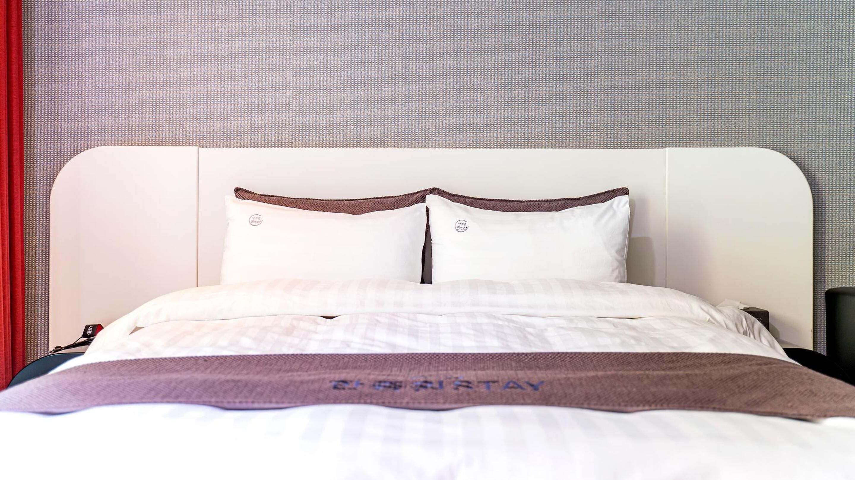 Un lit bien fait, avec une literie blanche et un coussin décoratif marron, une tête de lit et un mur orné d’un motif texturé.