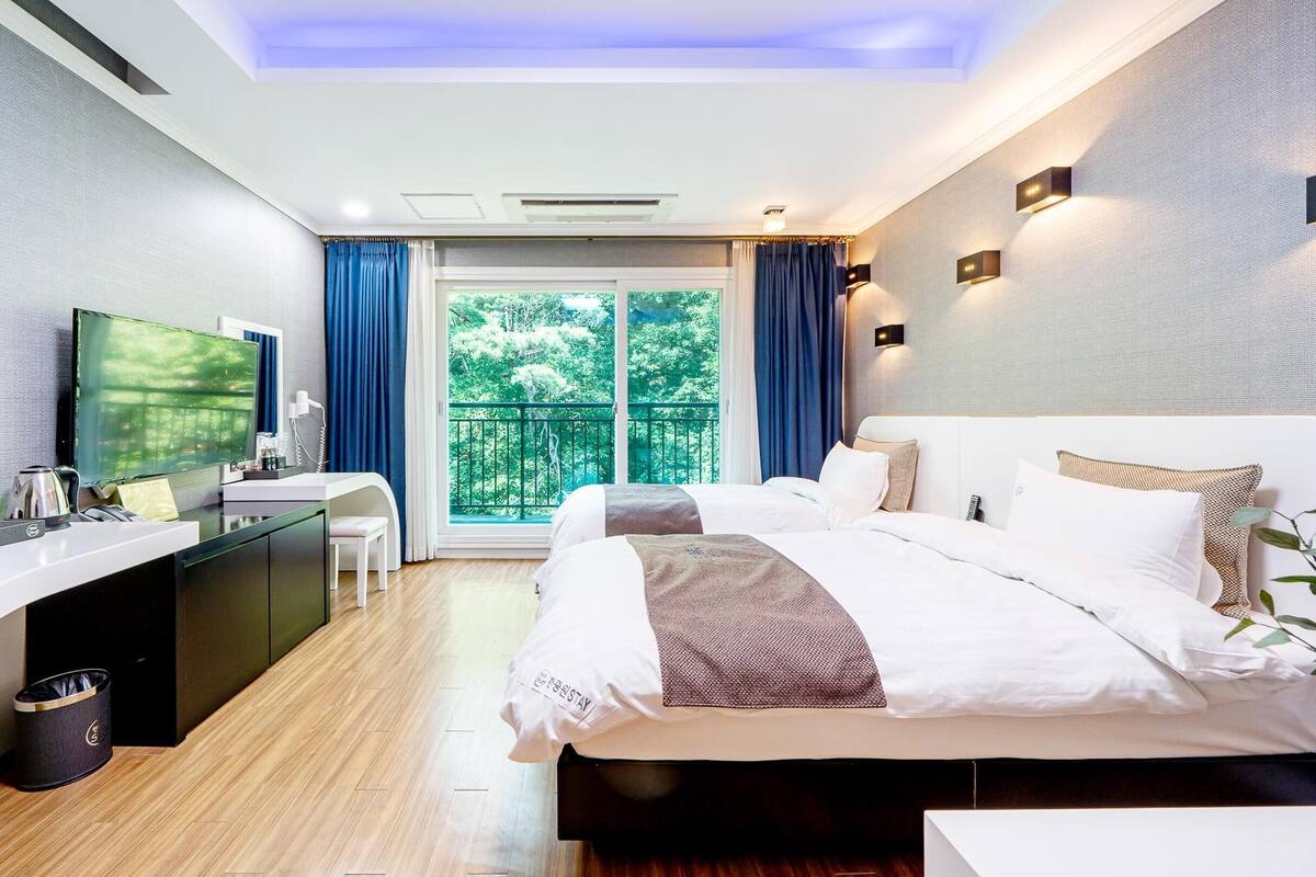 Ein modernes Hotelzimmer mit Bett, Schreibtisch und einem Balkon mit Blick auf Grünflächen.