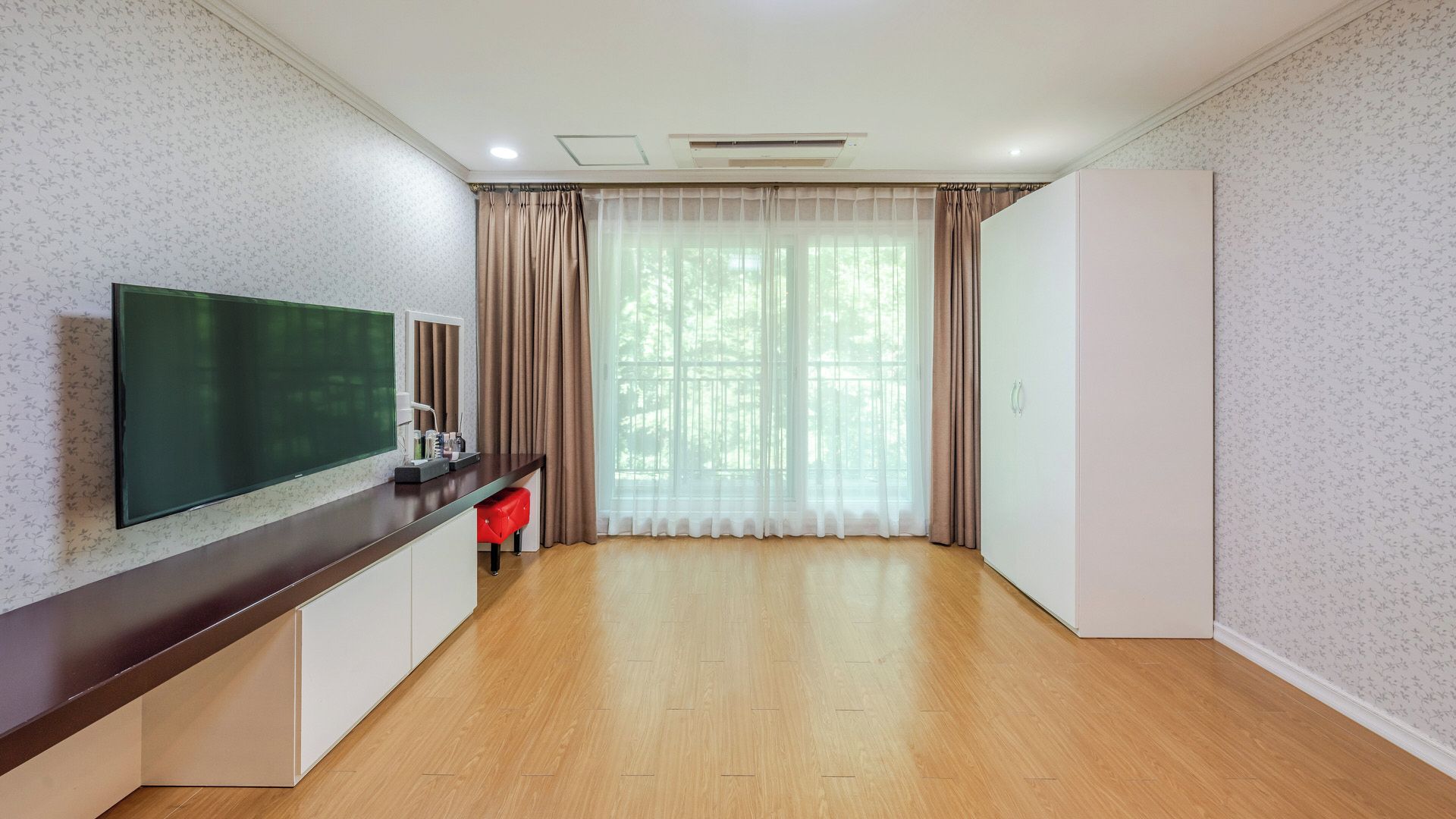Habitación de hotel con televisor de pantalla plana, escritorio con silla, armario y una ventana grande con cortinas.