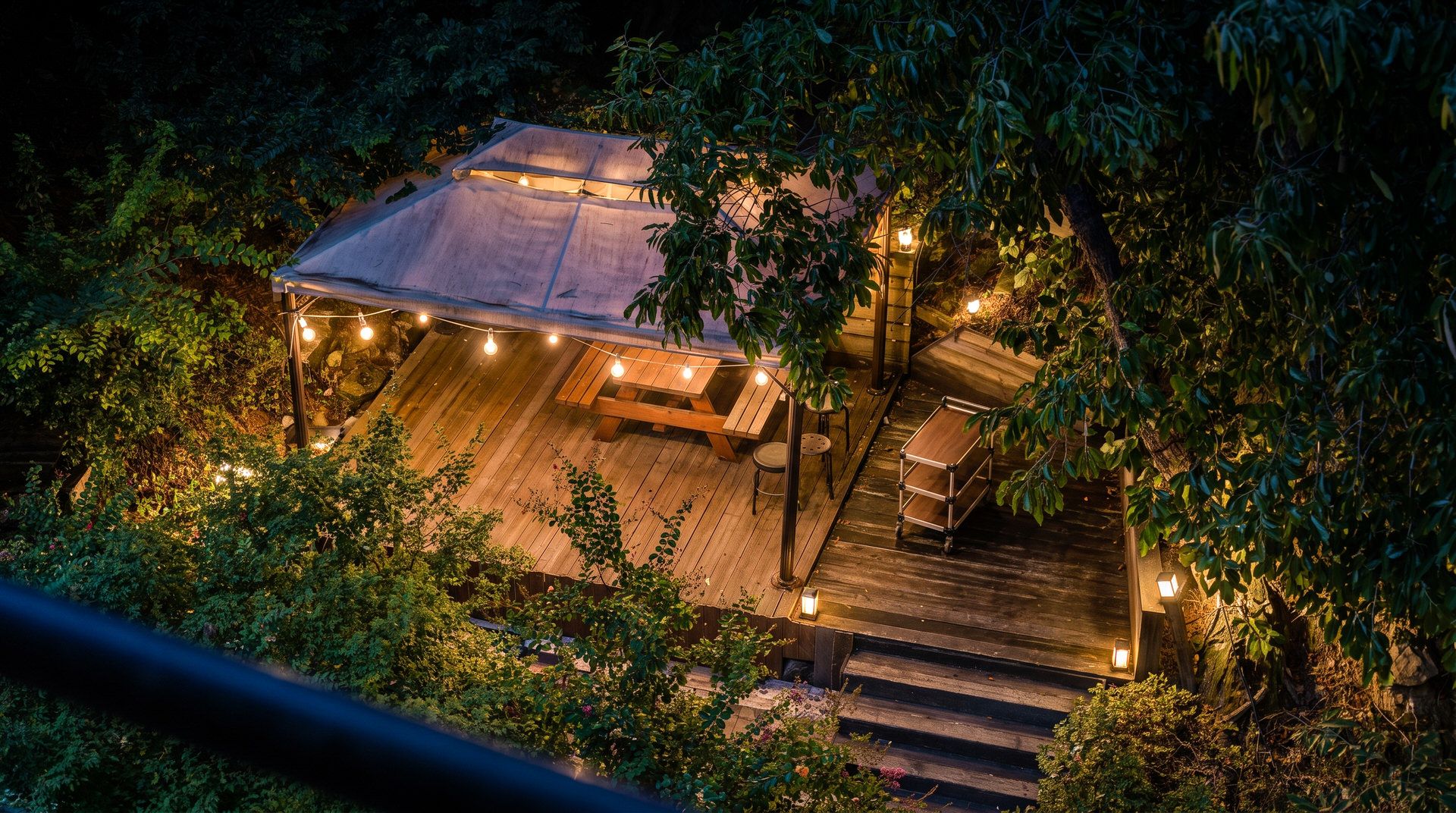 A rooftop patio with a wooden deck, string lights, and a table.
