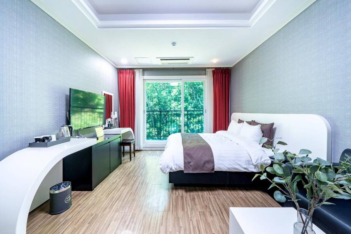 Ein modernes Hotelzimmer mit einem Bett, einem Schreibtisch und einem großen Fenster mit roten Vorhängen.