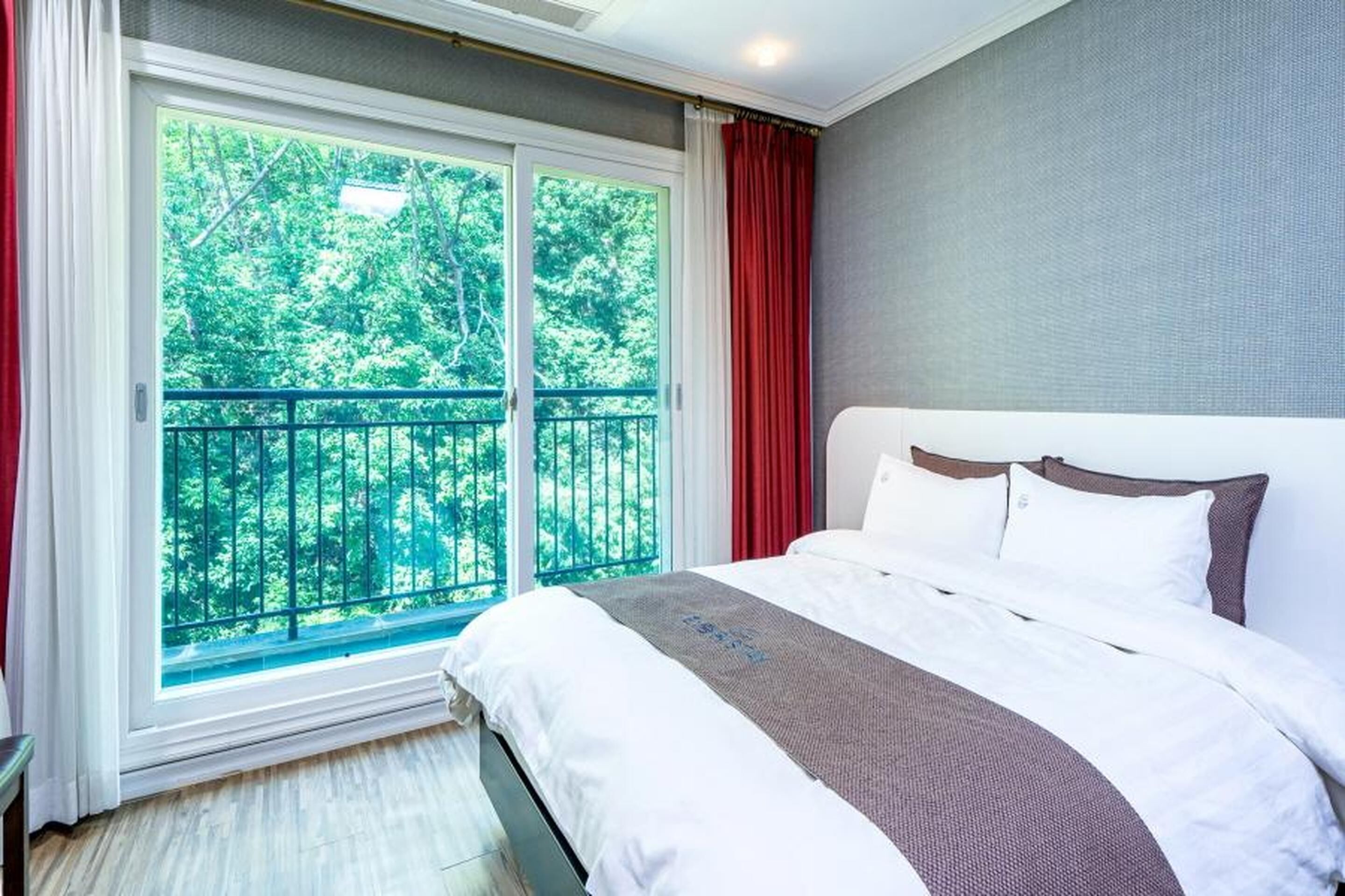 Ett hotellrum med ett stort fönster, en säng med vita och bruna sängkläder och en grå vägg.