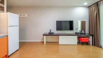 Una cocina compacta con refrigerador, un televisor de pantalla plana montado en la pared y una mesa de comedor de madera con una silla roja.