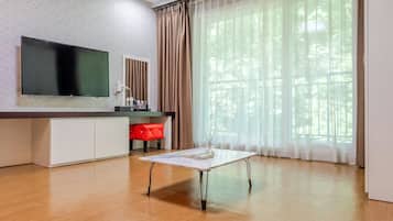 A modern living room with a flat-screen TV, a white coffee table, a red chair, and a large window with sheer curtains.