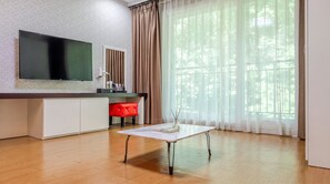 A modern living room with a flat-screen TV, a white coffee table, a red chair, and a large window with sheer curtains. - Namwon Hanjeungwonstay Pension (Namwon)